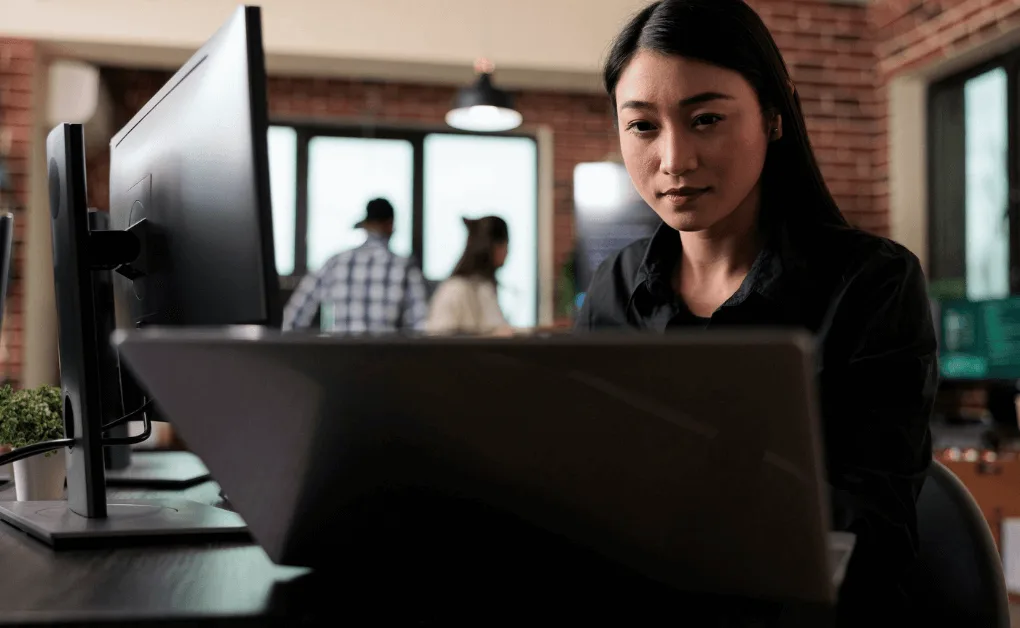Focused female developer working on a laptop in a modern tech office